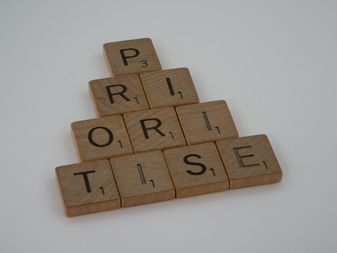 my-qualifications Close-up of wooden Scrabble tiles spelling 'prioritise' on a white surface, set in a pyramid shape.